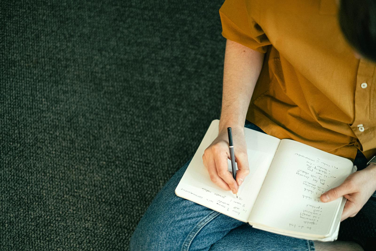 Close-up of a person taking notes in a notebook while sitting on the floor, emphasizing education and focus.