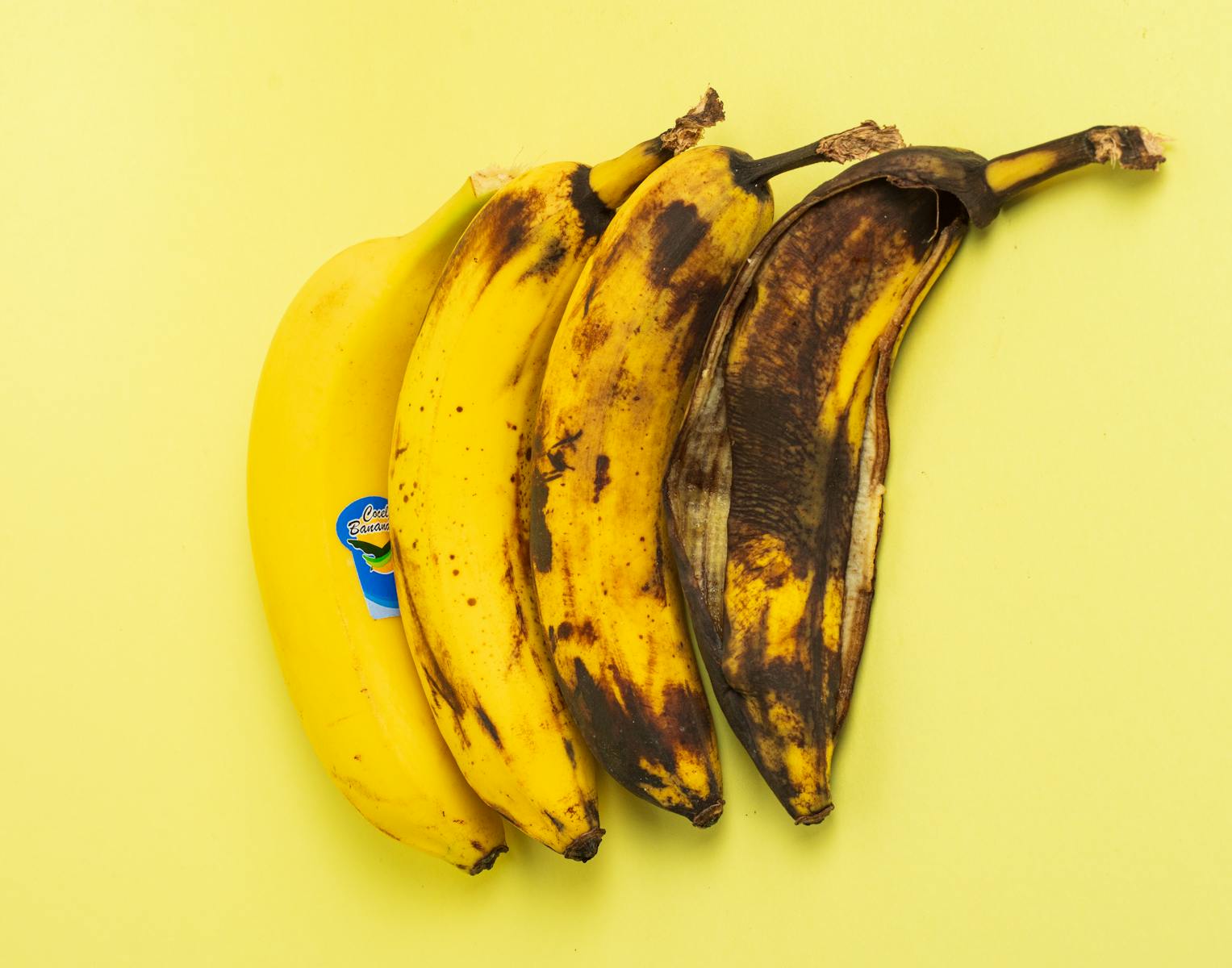 Four bananas showing ripening stages on a yellow background. Ideal for food, nutrition, and lifestyle themes.