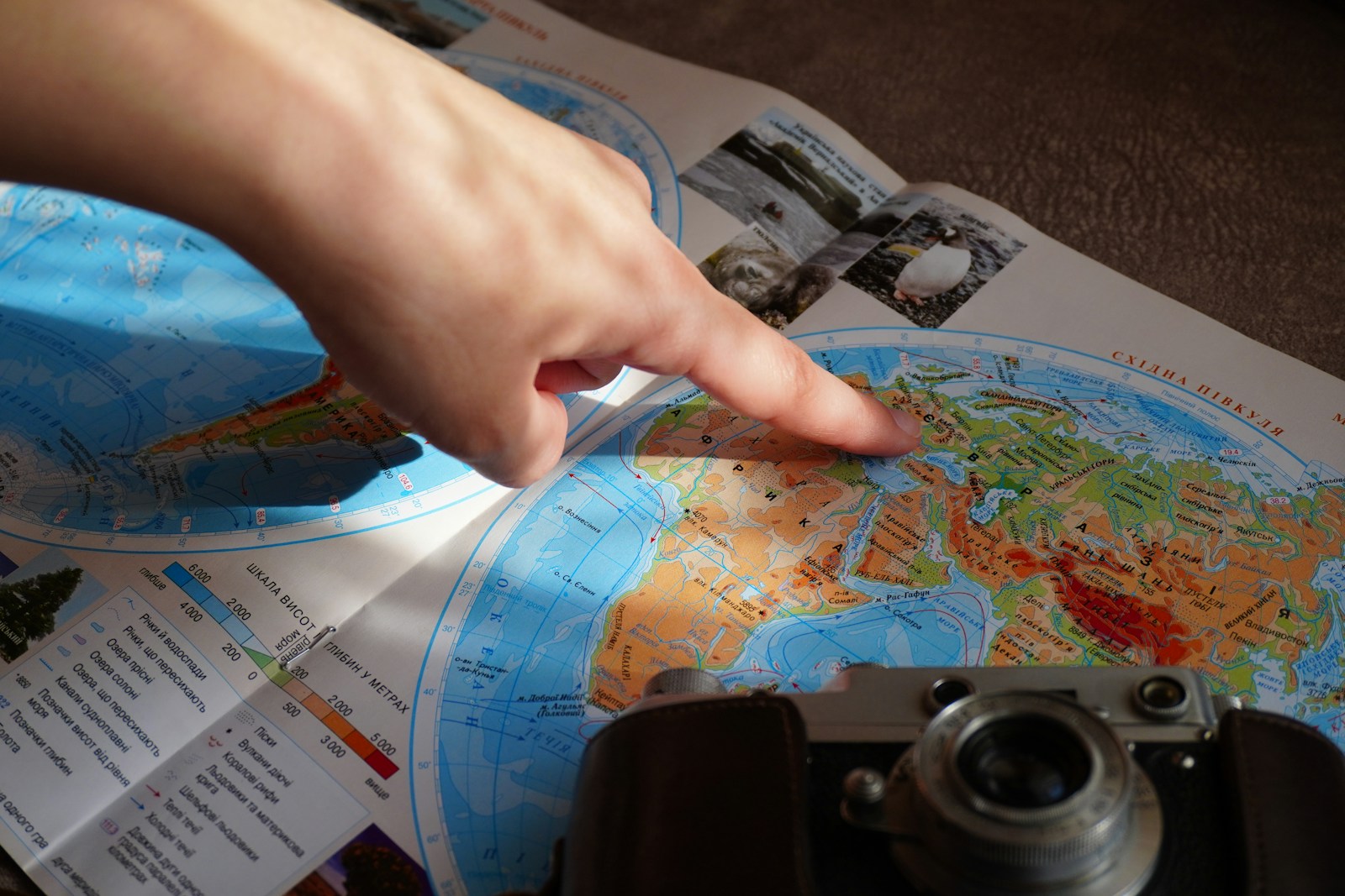 Finger pointing at a world map near a camera.